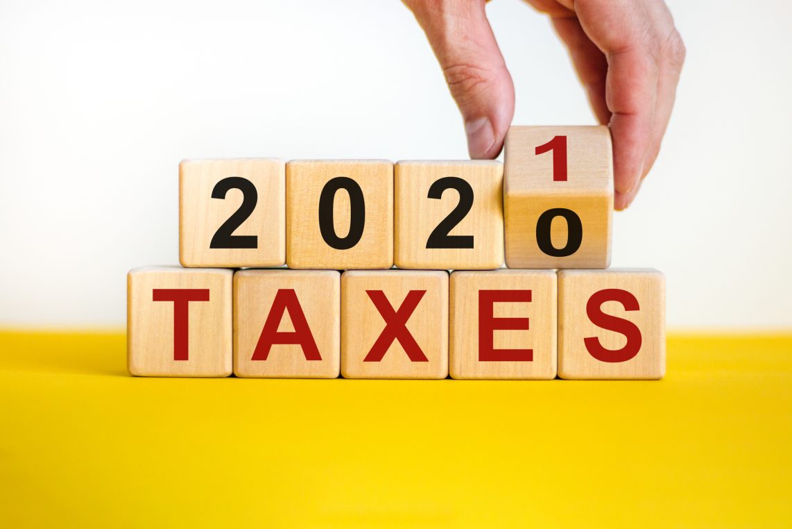 Business concept of planning 2021. Male hand flips wooden cube and change the inscription 'Taxes 2020' to 'Taxes 2021'. Beautiful yellow table, white background, copy space.